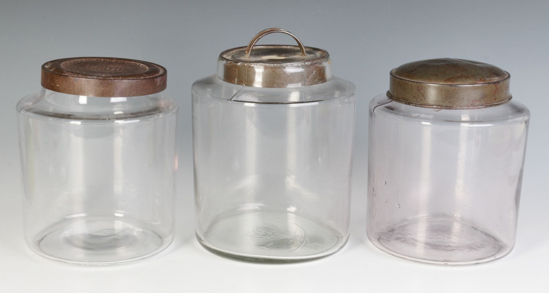 THREE EARLY BLOWN GLASS STORAGE JARS WITH TIN LIDS