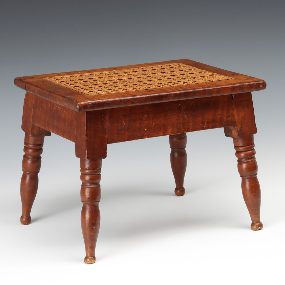 A 19TH CENTURY TIGER MAPLE CRICKET STOOL WITH CANING