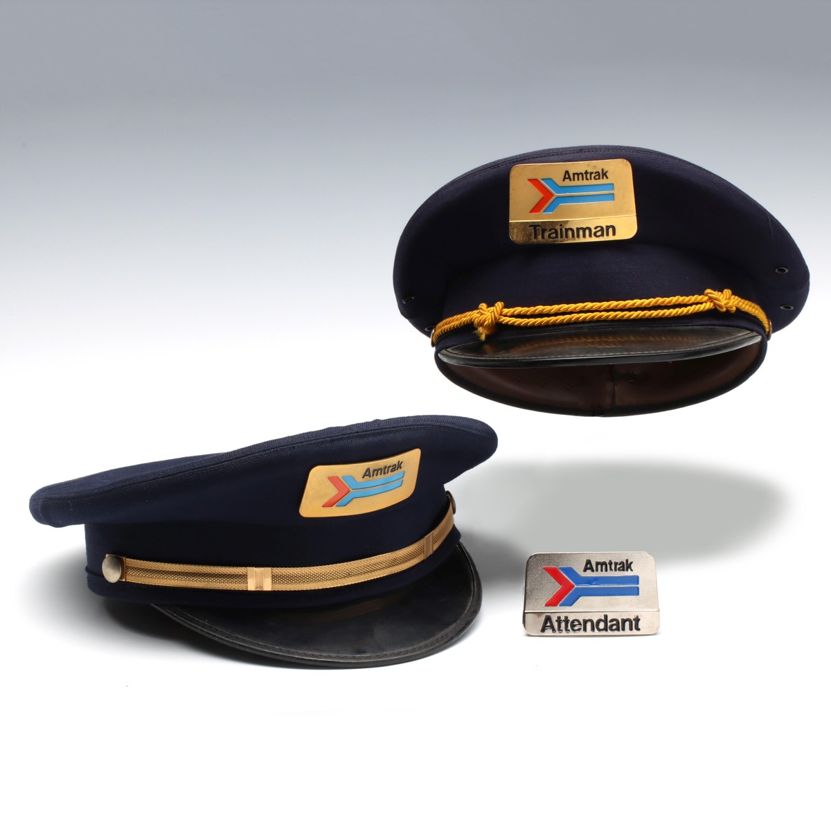 TWO AMTRAK VISOR CAPS AND AN ATTENDANT'S BADGE